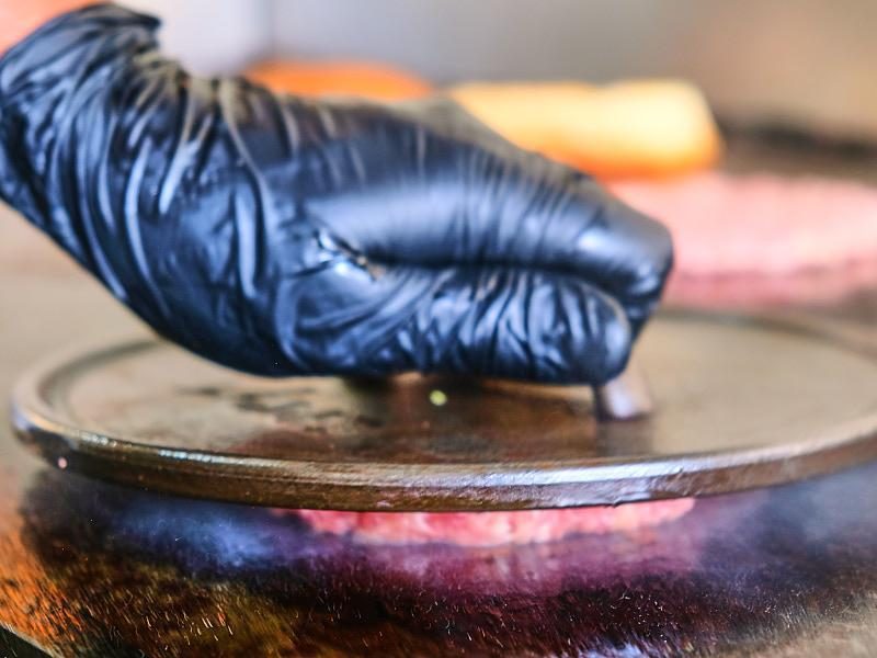 Guante negro prensando la carne sobre la plancha.
