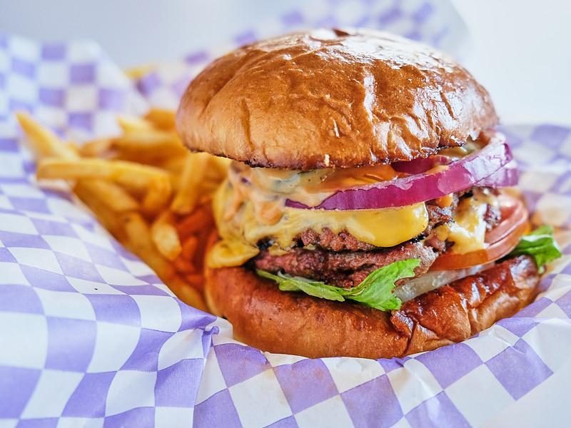 Doble smash burger con cebolla morada y papas sobre papel de cuadros.