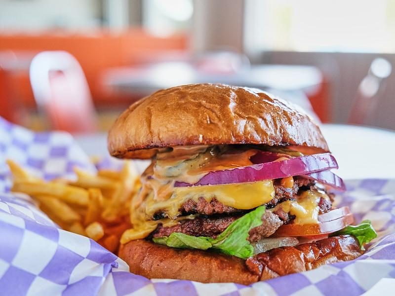 Doble smash burger con papas sobre papel de cuadros morados, adentro del local.