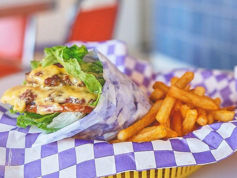 Burger envuelta en papel de cuadros morados con papas.