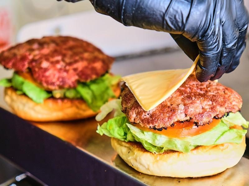 Dos burgers armándose, una con la carne y otra con el queso encima.
