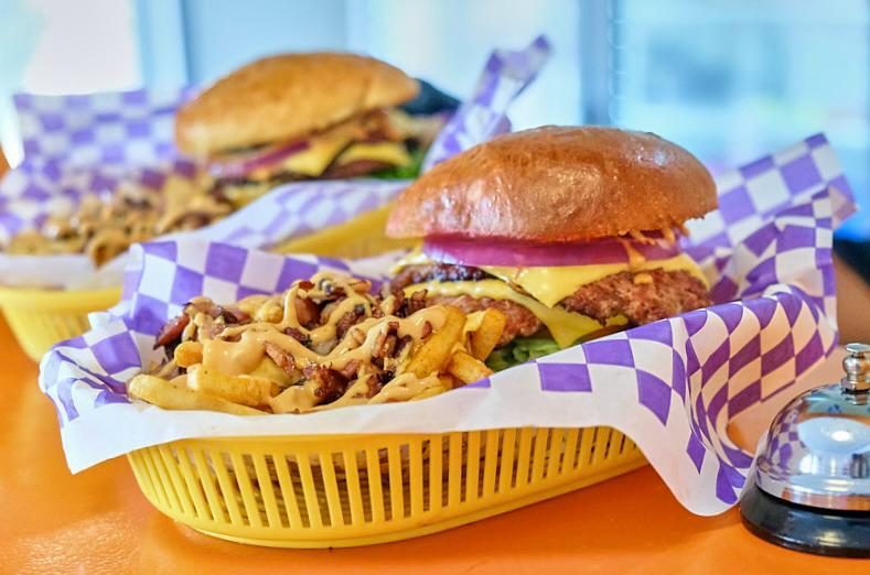 Canasta amarilla con burger y papas sobre papel de cuadros.