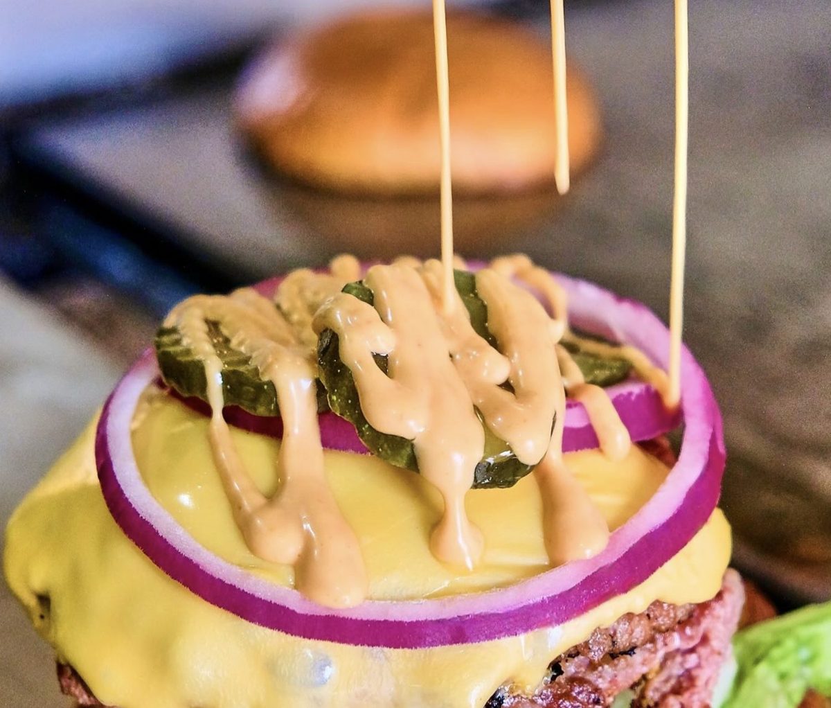 Smash burger de El Bajón con el aderezo especial escurriendo sobre el queso, pepinillos y cebolla morada.